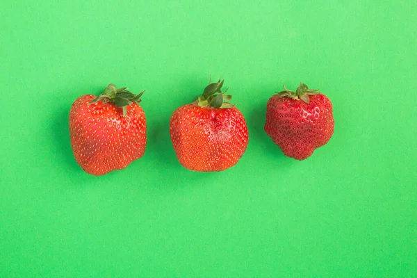 Άσχημο Φαγητό Τρεις Φράουλες Στο Κέντρο Του Πράσινου Φόντου Στο — Φωτογραφία Αρχείου