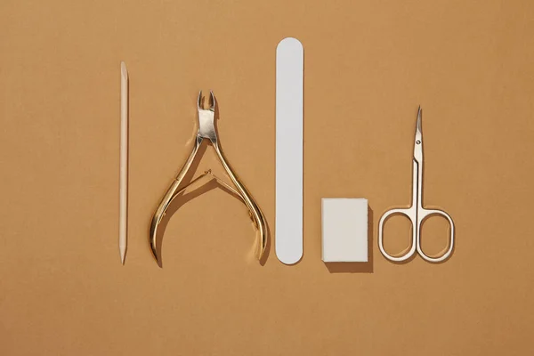 Manicure tools are laid out in one line in the center of the frame. cosmetic accessories for nails, scissors, pusher cuticle  and nail file. Top view of manicure tools isolated on brown. manicure at home concept. top view.