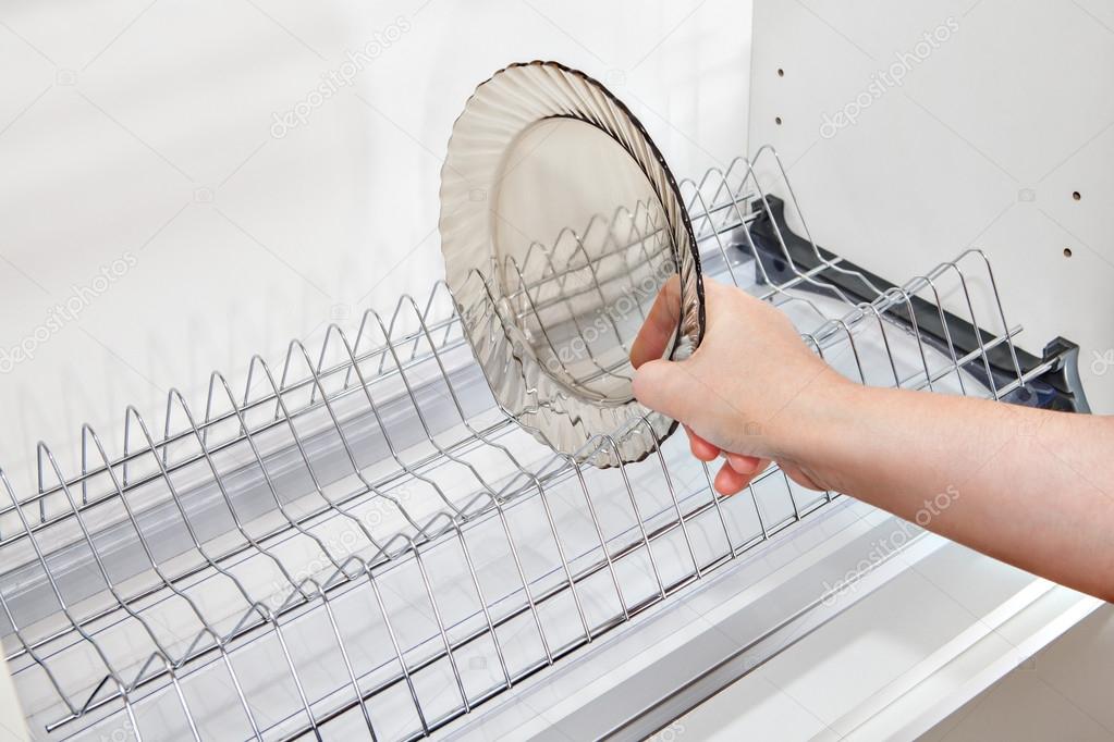 Close-up woman hand takes dish from inside wire plate drainer.
