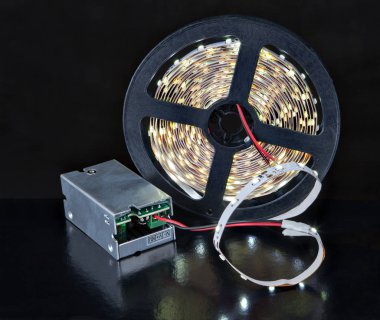 Close-up shine LED Light tape on spool and voltage adapter.