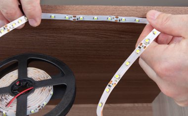 Close-up of hands handyman paste LED tape inside the cabinet.