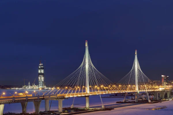Zimní noci ve městě, kabelový most přes zamrzlou řeku. — Stock fotografie