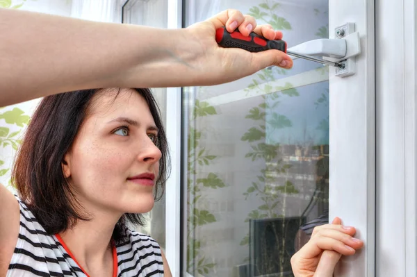 La chica desmonta la manija de la ventana usando un destornillador . — Foto de Stock