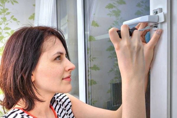 Mujer joven desenrosca una manija de ventana usando destornillador . —  Fotos de Stock