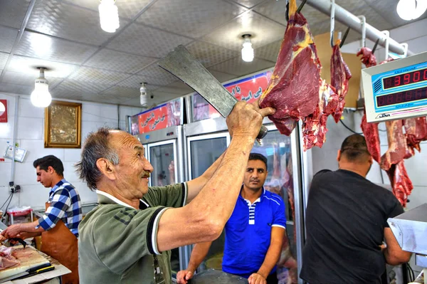 Carniceiro iraniano sênior cortando carne de cordeiro com faca no açougue . — Fotografia de Stock
