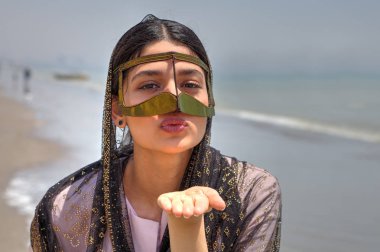 Girl in mask bandari woman sends air kiss, Southern Iran. clipart