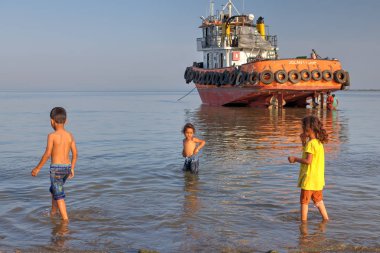 Girls and boy playing on shallows of Persian Gulf. clipart