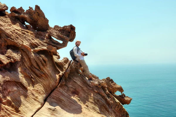 Turistické s kamerou sedí na okraji útesu. — Stock fotografie