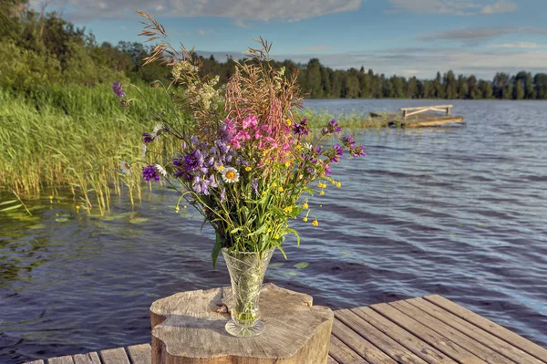 Ramillete de flores silvestres en un jarrón de cristal cerca del lago del bosque . — Foto de Stock