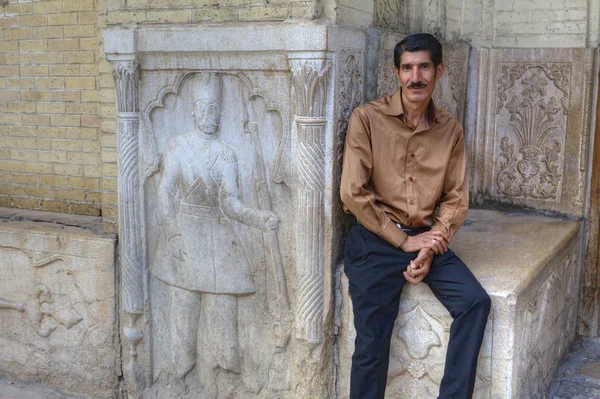 Iranska vuxen sitter på stenbänken nära gatan basrelief, Shiraz, Iran. — Stockfoto