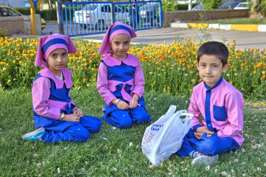 Anaokulu çocukları parkta çimlerin üzerinde oturuyorlar, Şiraz, İran.