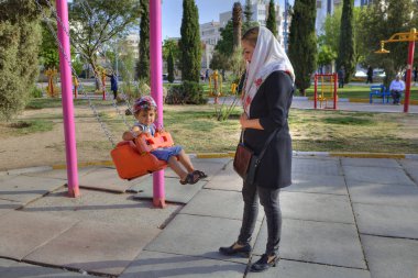 Anne sallanan küçük çocuk parkta sallanıyor, Shiraz, İran.