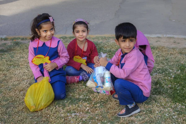 Pembe üniformalı anaokulu çocukları, parkta çimlerin üzerinde oturuyorlar, Şiraz, İran.