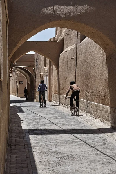 Iranska pojkar rida cyklar längs smala välvda gränd Yazd, Iran. — Stockfoto