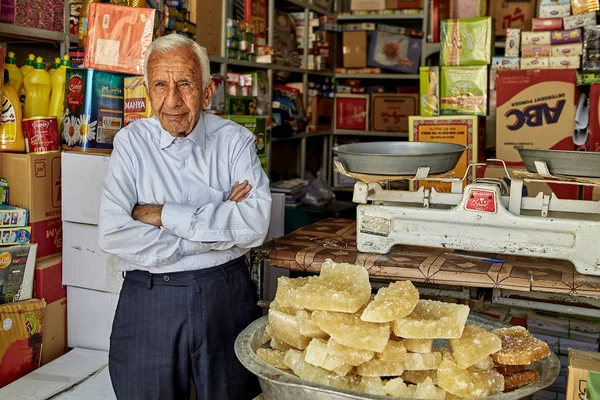 An elderly Iranian grocer stands at entrance to food store. — Stock Photo, Image