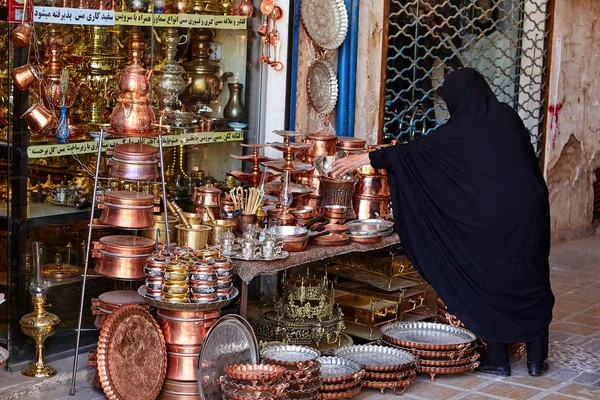 Женщина, одетая в исламскую вуаль, покупает медную посуду на базаре . — стоковое фото