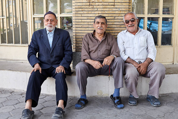 Пожилые люди сидят на бетонном фундаменте здания, Кашан, Иран
