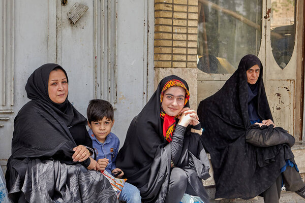 Мусульманские женщины с ребенком сидят на автобусной остановке, Кашан, Иран
.