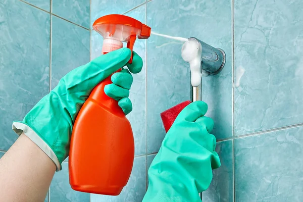 Hand in green glove holds cleaning agent with foam spray.