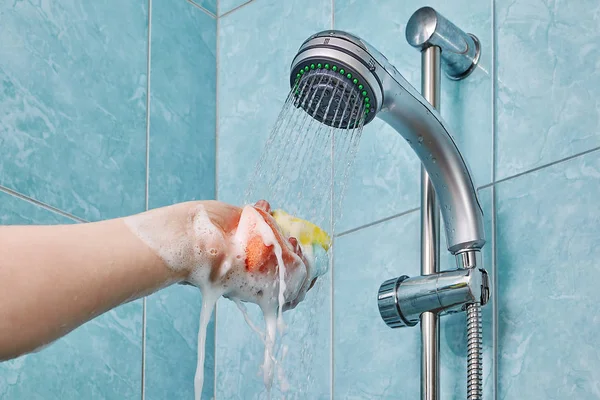 Multicolor Schwamm in menschlicher Hand unter dem Duschkopf zusammendrücken, Nahaufnahme. — Stockfoto