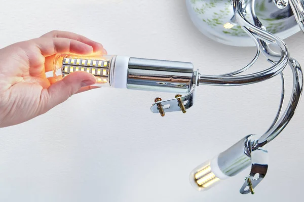 Hand is screwing LED corn lamp into room ceiling lighting. — Stock Photo, Image