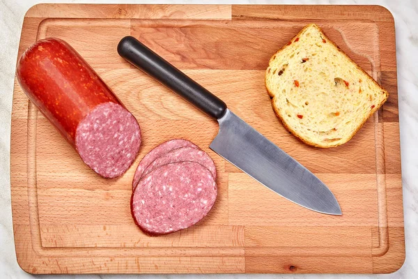 Szeletelt szalámi, kenyér és kés vágódeszkán. — Stock Fotó