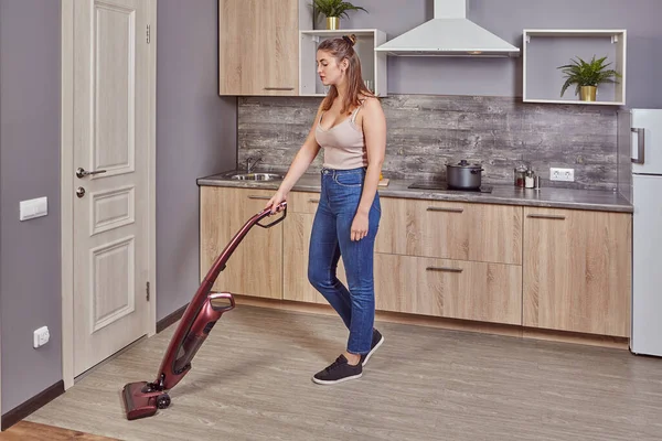 Giovane cameriera bianca è aspirapolvere pavimento in cucina — Foto Stock