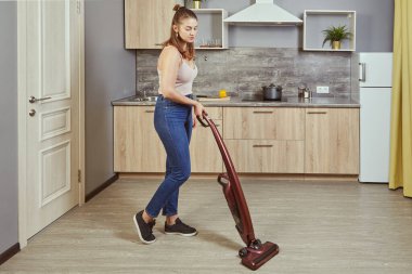 Genç beyaz kadın kablosuz elektrik süpürgesi ya da elektrikli süpürge kullanarak mutfakta temizlik yapıyor. 22 yaşında beyaz bir kadın bir dairede temizleniyor..