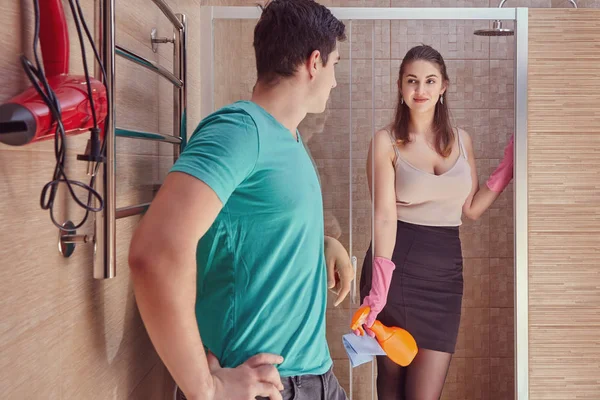 An employer flirts with a cleaning lady in bathroom. Sexual harassment in the workplace, discrimination against women. Sexy young maid is cleans the shower room under the supervision of a white man.