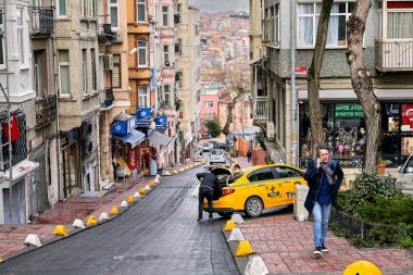İstanbul, Türkiye - 12 Şubat 2020: Beyoğlu bölgesinde dar bir sokak, yoldan geçen bir erkek telefonla konuşuyor, bir taksi şoförü bagajı açtı.