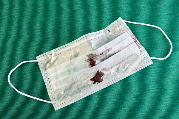 Blood stains on a disposable face mask, close-up, green background.