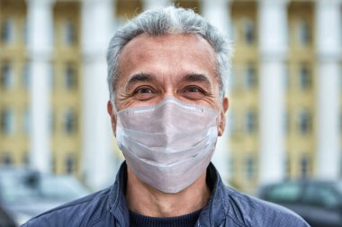 Coronavirus covid-19 salgınında tek kullanımlık koruyucu cerrahi maske takmış gülümseyen beyaz beyaz adam sokaklarda yürüyor..