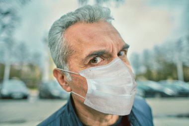 Coronavirus covid-19 salgınında sokakta yürüyen, tek kullanımlık koruyucu yüz cerrahi maskeli, beyaz, olgun bir adamın portresi..