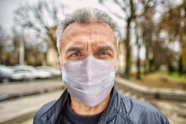 Coronavirus covid-19 salgını sırasında korunmak için tek kullanımlık yüz maskesi takan ciddi bir olgun adamın portresi..