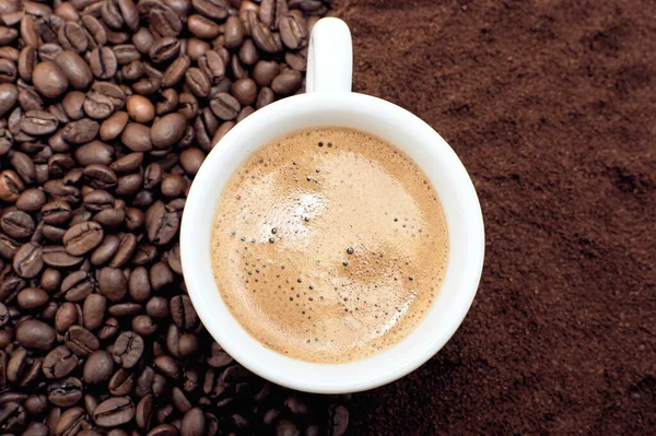 A cup of fresh coffee with foam. Background of coffee beans and ground coffee.
