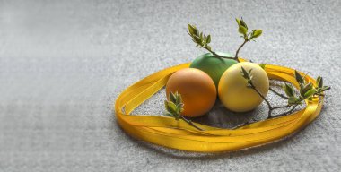 Renkli yumurtalarla Paskalya kompozisyonu, sarı bir kurdele, genç yapraklı dallar.