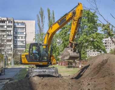 Excavator digs land between residential buildings clipart