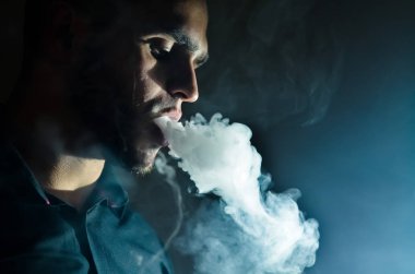 Elektronik sigara içen genç adam. Elektronik bir sigarayı dumanla buharlaştırmak. Vape konsepti alanı kopyala Seçici odak.