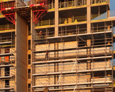 builders working on scaffolding and platforms on different floors of a large modern construction site