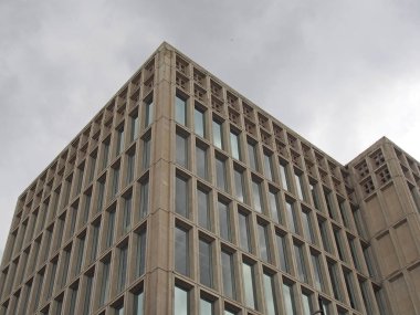 Gri bulutlu gökyüzüne karşı geometrik beton iskeleti olan 1960 'ların tipik vahşi tarzı bir beton ofis binasının köşesi.
