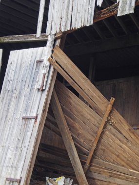 close up of an abandoned collapsing wooden building made of brown timber with scattered planks and door