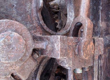 a close up of rusted iron connecting rods and gears with bolts on old corroded machinery