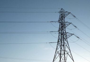 a tall electricity pylon with multiple high voltage cables silhouetted against a blue sky