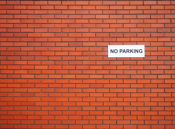 Fehér tábla, hogy tilos parkolni a vörös téglafalon. — Stock Fotó