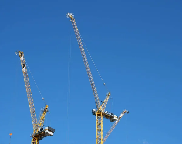 Two tall yellow construction cranes working against a blue sky — Stok fotoğraf