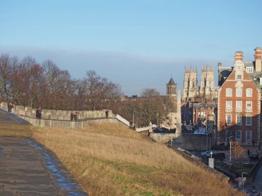 people walking along the city walls in york with the minster and buildings of the city in the distance