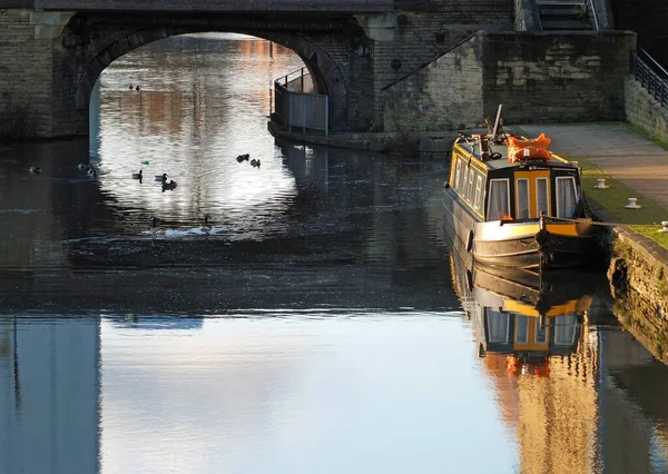 Un vieux bateau étroit traditionnel amarré sur le canal près du bassin de la maison lumineuse dans le yorkshire occidental avec des canards nageant sous un vieux pont en pierre — Photo