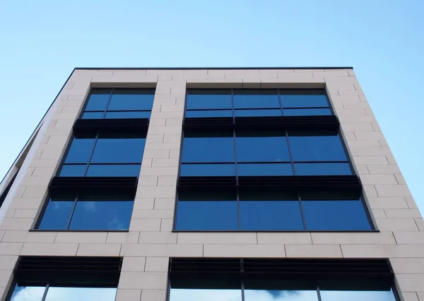 Upwards view of the facade of a modern office buildings with blue sky reflected in the rows of geometric windows — 스톡 사진