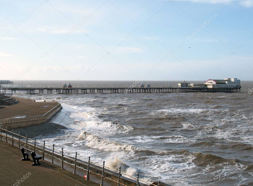 A view of the south pier at blackpool with the sea in front of the promenade and seagulls flying in a blue sunlit sky
