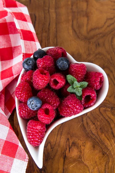 Blueberries and raspberries in the white dish on wood — Stock Photo, Image